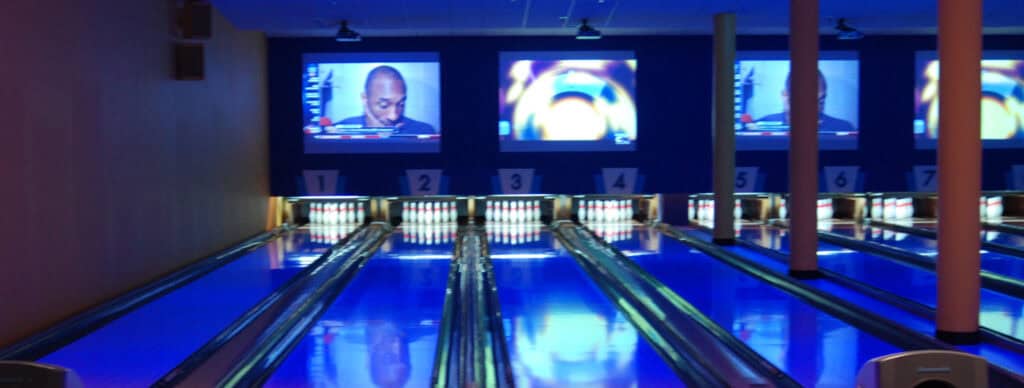 bowling lanes lit with blue light with TVs above the back of them