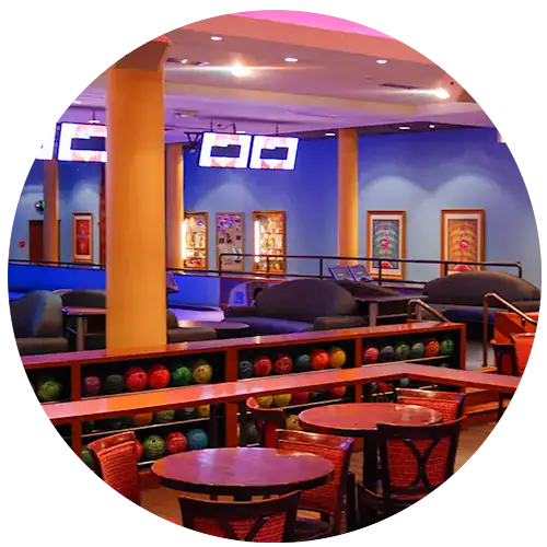 Colorful bowling balls on a wood rack with cocktail tables in the front. Art hangs on walls in the background.
